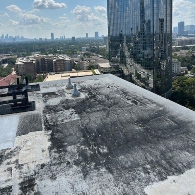 View from a building rooftop showing a weathered surface with scattered vents, overlooking a city skyline with high-rise buildings and a large glass tower reflecting the surroundings. An area marked for asbestos sampling highlights the importance of safety in urban settings.